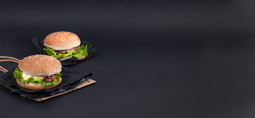 Two hamburger on a black background for lunch. Fast food and snacks. Free space for text. Copy space. Flat lay. Banner.