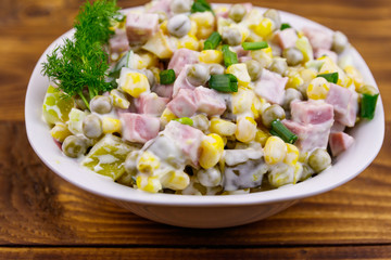 Tasty salad with sausage, green pea, canned corn, bell pepper, cucumber and mayonnaise on wooden table