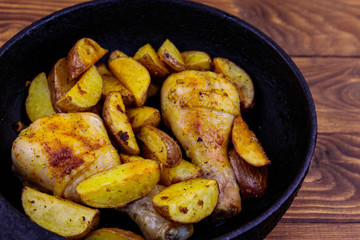 Baked chicken drumsticks with potatoes in cast-iron frying pan on wooden table