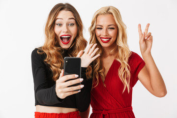 Two girls friends isolated over white wall dressed in black and red clothes using mobile phone...