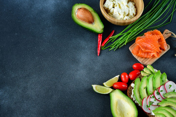 sandwich with avocado and salmon on a dark background, green onions and gluten-free grain bread, radishes and tomatoes. concept diet food, copy space, sandwich take away, healthy fast food