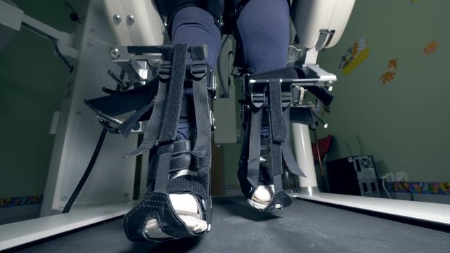 Legs of a physically challenged person tied with belts are moving along the walking track