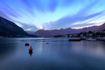 Long exposure sunset in bay of Kotor Montenegro.   Water appears flat, and wispy cloud effect, in a bay surrounded by jagged glowing mountain. blue hour capture 
