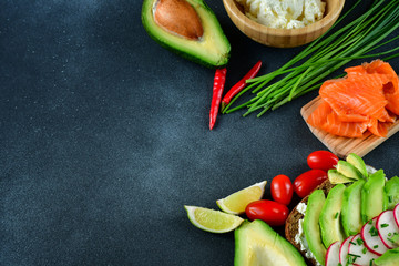 sandwich with avocado and salmon on a dark background, green onions and gluten-free grain bread, radishes and tomatoes. concept diet food, copy space, sandwich take away, healthy fast food
