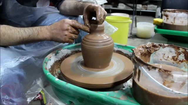 A Bulgarian craftsman with 14 years of experience on a potter's wheel removes liquid clay slip with a tool foam sponge. reporting shooting