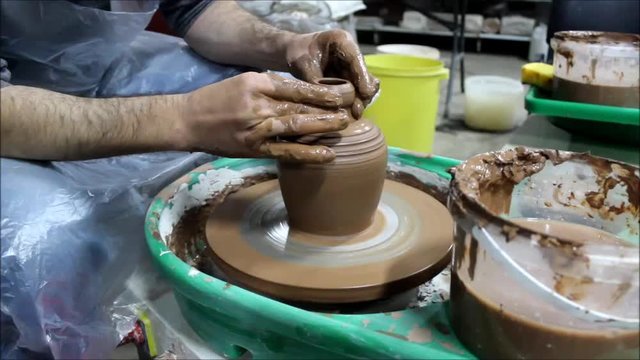 A Bulgarian craftsman with 14 years of experience on a potter's wheel removes liquid clay slip with a tool foam sponge. reporting shooting.