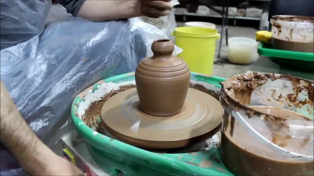 A Bulgarian craftsman with 14 years of experience on a potter's wheel removes liquid clay slip with a tool. reporting shooting