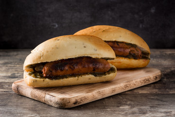 Choripan. Traditional Argentina sandwich with chorizo and chimichurri sauce on wooden table