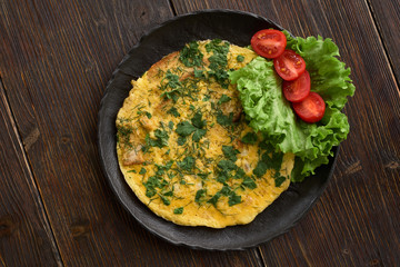 omelet with croutons on a black plate, wooden table