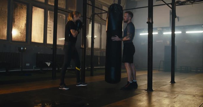 WS Female boxer hitting a huge punching bag at a boxing studio. Woman boxer practicing with boxing trainer. 4K UHD
