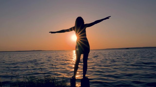 Silhouette Of Young Woman Raised Her Hands Up And Side At Sunset On The Sea