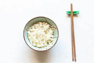 cup with rice and chopsticks on rest on white