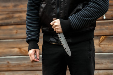 A man, a criminal in black clothes, holds a large knife in his hand. Close-up, copy space. The...