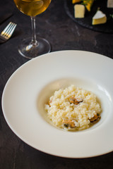 risotto with mussels (seafood rice) in a white plate and a glass of white wine on a dark background