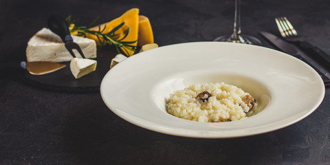 risotto with mussels (seafood rice) in a white plate and a glass of white wine on a dark background