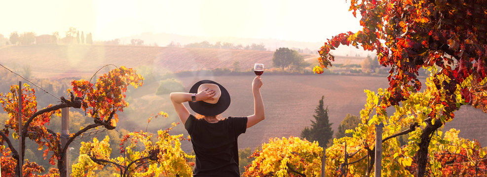 Girl in a hat at sunset and a glass of wine in hand. Nature Italy, hills and grape fields the sunlight. Glare and sun rays in the frame. Free space for text. Copy space.