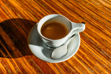 White Cup of Espresso Shining in the Sun on a Wood Table