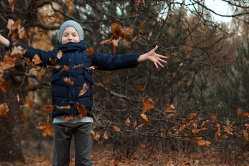 A pile of autumn, yellow foliage, a child, a boy playing with foliage in a park, throws up leaves. Concept autumn, yellow leaves, autumn mood. Copy space.