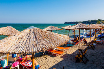People, tourists under umbrellas with loungers placed next to the coastline
