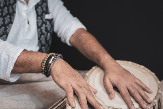 Images of a man's hands (wearing beads) playing the Tabla - Indian classical music percussion instrument - black background.
