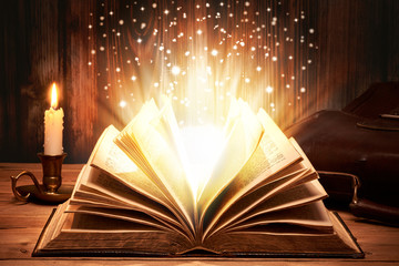 Altes Buch mit magischen Lichtern auf Holztische bei Kerzenschein