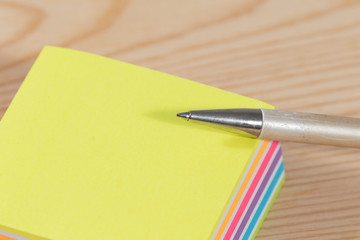 silber ballpen on top of a stack of sticky notes on wooden table 