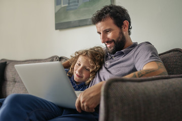 Father and son sitting at home watching a movie online