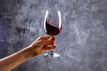 Close up of female arms swirling wineglass with expensive pinot noir wine in one hand against light grunged concrete wall background. Cropped shot, copy space for text.