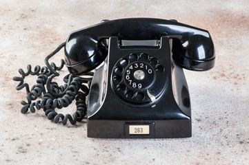 Antique black rotary phone on concrete background.