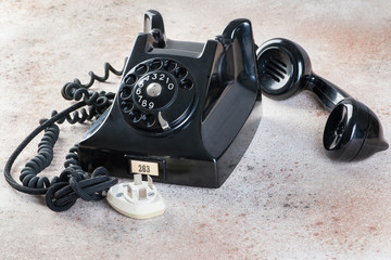 Antique black rotary phone on concrete background.