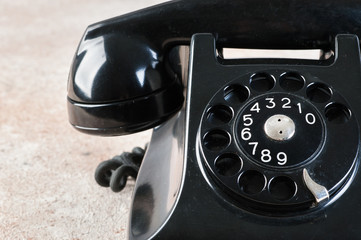 Antique black rotary phone on concrete background.