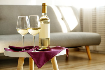Vintage bottle of white wine with blank matte label and two glasses on purple napkin, lofty interior background. Expensive bottle of shardonnay concept. Copy space, top view, flat lay, close up.