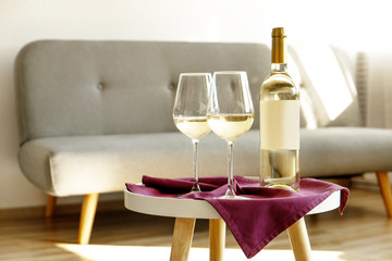 Vintage bottle of white wine with blank matte label and two glasses on purple napkin, lofty interior background. Expensive bottle of shardonnay concept. Copy space, top view, flat lay, close up.