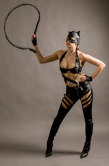 Young woman wearing a cat suit and mask with a whip