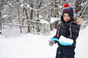 Fototapeta na wymiar A cute little boy throws snow in the winter snow-covered forest, trees in the snow. enjoys the winter. plays snowballs. happy, smiling, laughing