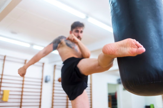 Male boxer workout high kick on the punching bag in gym.