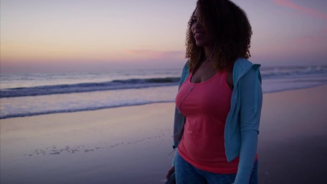 Afro hair Ethnic African American female doing exercise wearing sportswear on the beach and walking to music with ear buds  