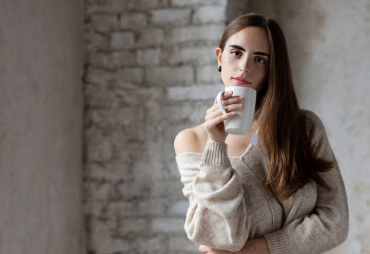Girl with long brown hair looks towards the camera and holds a breverage with a pleasant face expression