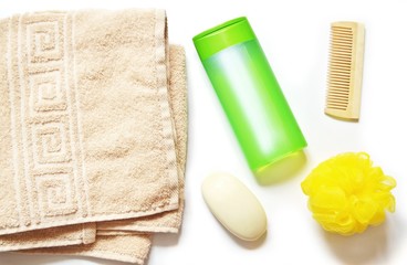 Beige towel, green shampoo bottle, soap bar, wooden comb and yellow sponge