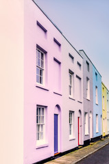 Bright colourful symmetrical row, terrace houses each with two sash windows and lunette arch above the doors