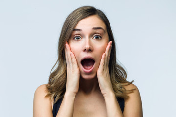Surprised young woman screaming and putting her hands on her face looking at camera isolated on white.