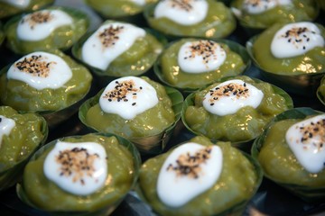Thai dessert sweet is Creamy Coconut Tapioca and Corn Pudding with Coconut Ta-go topping and wrapped with banana leaves on wooden background.