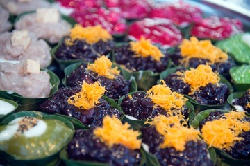 Thai dessert sweet is Creamy Coconut Tapioca and Corn Pudding with Coconut Ta-go topping and wrapped with banana leaves on wooden background.