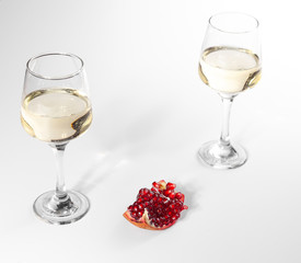 Broken pomegranate lies on a white plate. Two glasses of white wine.