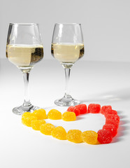 A glass of white wine. Multi-colored candies on a white background.