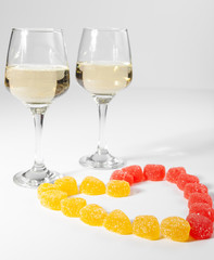 A glass of white wine. Multi-colored candies on a white background.