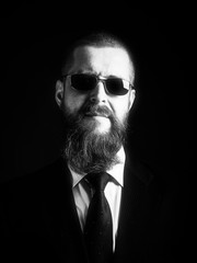 Obraz premium Close up studio portrait of bearded hipster male in sunglasses over dark background. low key on the black background, black and white photo