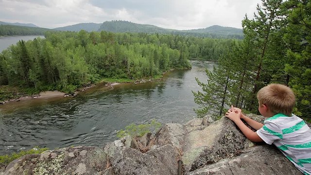 Summer landscape in the mountains . Girl teenager the artist paints sitting on a high cliff. rapid river flow. forest of trees, birches and pines. The girl looks at the rapid flow of the river