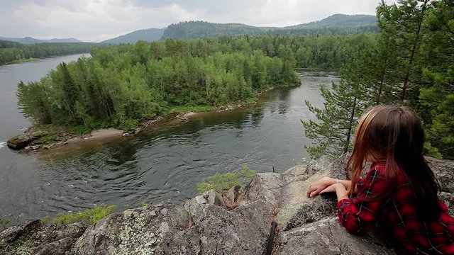 Summer landscape in the mountains . Girl teenager the artist paints sitting on a high cliff. rapid river flow. forest of trees, birches and pines. The girl looks at the rapid flow of the river