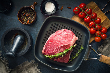 Raw Fresh Marbled Meat Beef on a grill pan ready for cooking on a blue concrete background top view.